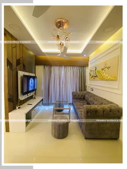 A full view of the living room in Majestic Villa, Dronagiri. The combination of a dark wood TV panel, a light-colored sofa, and warm ambient lighting creates a balanced and inviting atmosphere.