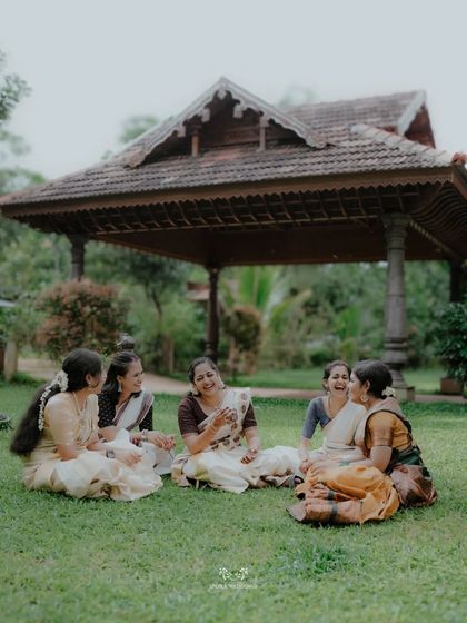 The bride and her friends sharing a laugh while sitting on the grass, a candid moment of friendship and joy.