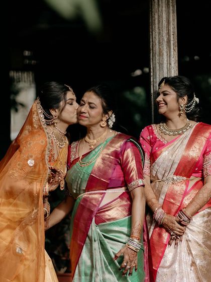 A tender moment as the bride kisses her mother, with her sister smiling beside them.