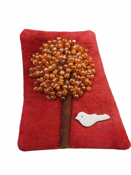 A unique fabric pin or patch depicting a tree with orange beads and a small white bird. This artistic accessory is a beautiful, handcrafted piece to adorn your attire.