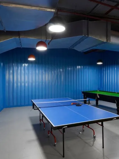 The "container" game room, with walls made of blue corrugated metal sheets to resemble a shipping container. The space includes a pool table and a ping pong table.