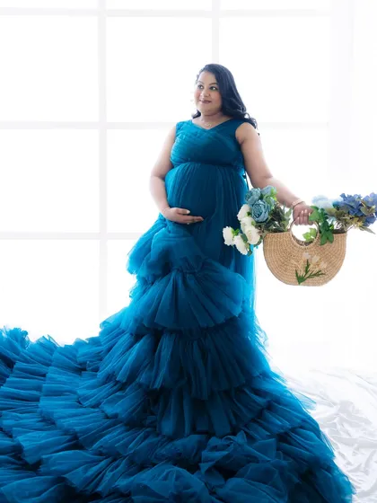 A bright and cheerful portrait of a mom-to-be in a blue ruffled gown, holding a basket of flowers.