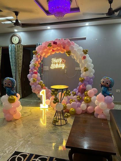 A sweet Cocomelon theme for a first birthday, using a pastel pink and purple color palette for a softer look. The setup includes a circular balloon arch, a light-up '1', and character balloon columns.