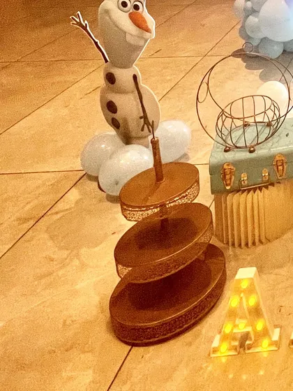 Thematic props are key to the experience. Here you can see a cute Olaf balloon figure next to a tiered dessert stand and a light-up marquee letter 'A'.
