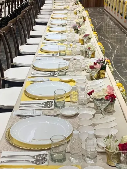 A long dining table meticulously set for a traditional feast. The combination of white and yellow linens, along with fresh flowers, creates a bright and welcoming atmosphere for guests.