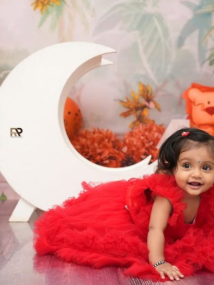 A baby girl crawls on the floor in a beautiful red dress, part of the jungle moon themed shoot. Her happy expression and the creative setup make for a memorable photo.