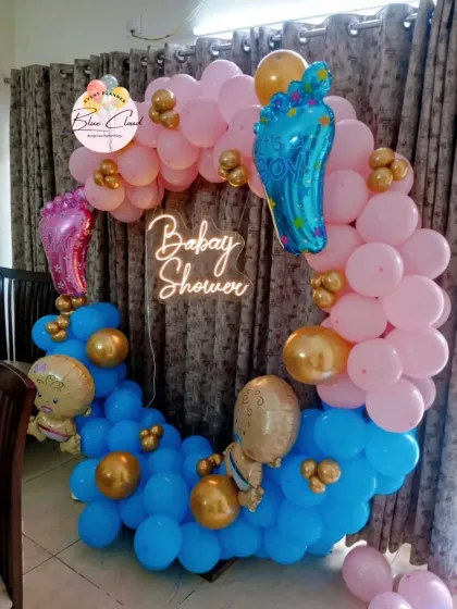 A gender reveal 'He or She' themed balloon ring with a neon 'Baby Shower' sign.