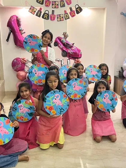 A group of happy kids proudly holding up the flamingo themed clocks they painted at Saisha's 9th birthday party. These custom art activities also double as a unique and personal return gift.
