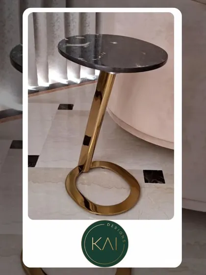 A sleek and modern side table with a black marble top and a polished gold base. The minimalist design, featuring an elliptical base, adds a touch of sculptural elegance to any room.