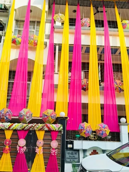 A full view of a multi-story house decorated with long, flowing drapes in pink and yellow. This kind of decoration instantly signals a celebration in the neighborhood.