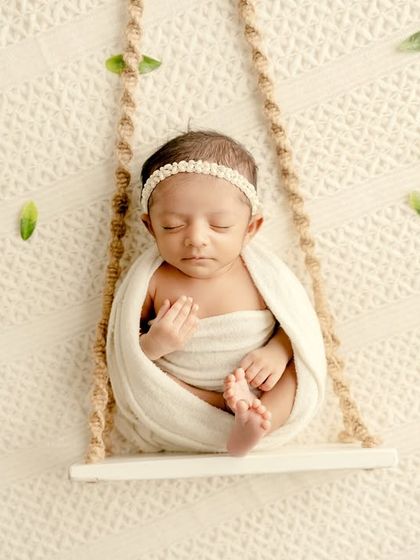A top-down view of the newborn on a swing, with scattered green leaves adding to the simple, organic beauty of the shot.