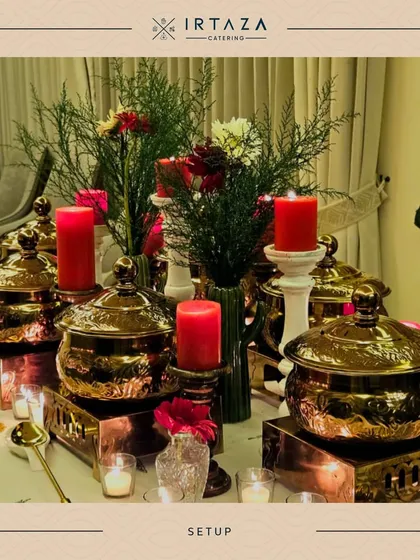 A beautiful arrangement for a home catering event. The combination of hammered copper pots, fresh greenery, and red candles on a white tablecloth creates a warm and inviting feel.