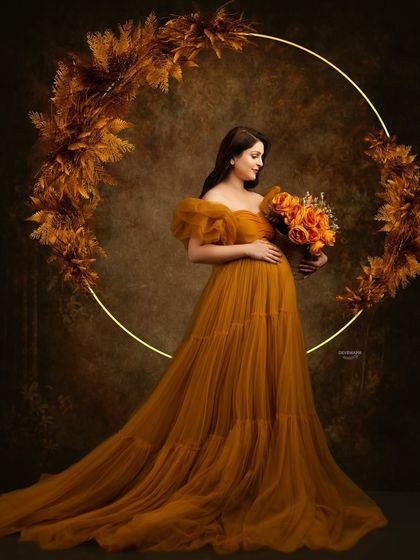 A warm, autumnal-themed portrait. The client wears a beautiful mustard-colored tulle gown, framed by a lit ring decorated with pampas grass for a rustic and elegant look.