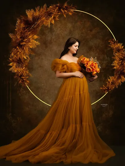 A warm, autumnal-themed portrait. The client wears a beautiful mustard-colored tulle gown, framed by a lit ring decorated with pampas grass for a rustic and elegant look.