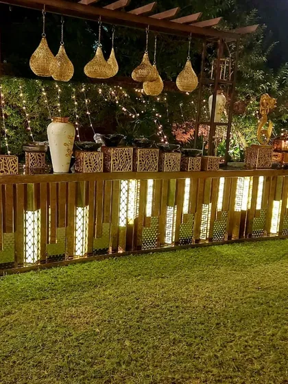 An elegant outdoor catering setup for an evening event. The warm lighting on the wooden counters, combined with decorative vases and hanging lamps, creates a welcoming and sophisticated ambiance for guests.