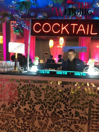 A bartender at a 'Cocktail' station with a vibrant mosaic bar front and disco balls hanging from the ceiling.