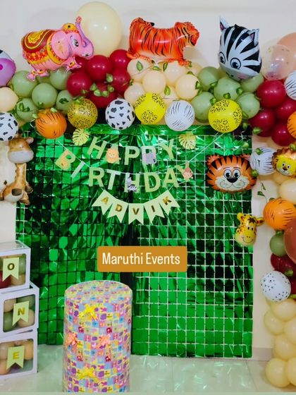 A jungle-themed first birthday with a shiny green foil backdrop. The decor is filled with animal balloons, including a tiger, elephant, and zebra, and fruit-filled "ONE" blocks.