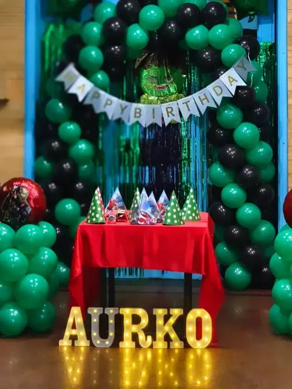A close-up of the cake table for the green and black themed party, showing the party hats and themed foil balloons.