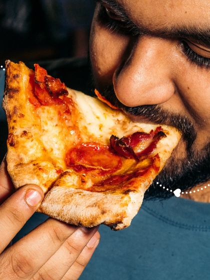 A close-up of a customer taking a big bite of a pepperoni pizza slice. It's all about that satisfying, flavorful experience.