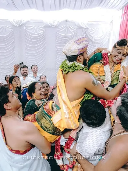 Capturing the fun and energy of wedding rituals. This candid shot shows the couple being lifted by family members during a traditional South Indian ceremony, full of laughter and celebration.