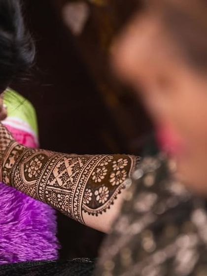 A candid shot of mehendi application in progress, showing the detail and focus required for bridal work.