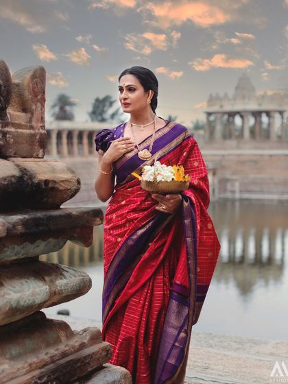 The grandeur of the temple surroundings is matched by the regal beauty of the red and purple Kanchipuram silk saree.