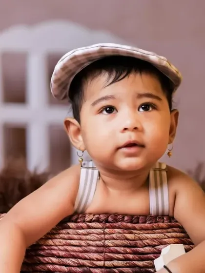 A close-up portrait of a baby boy in a basket, looking very stylish with his flat cap.