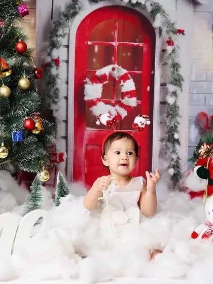 This little girl celebrates turning one with a playful expression in a beautiful, snowy Christmas scene.