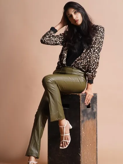 A chic, modern look pairing an animal print top with olive green leather pants. The makeup is kept neutral and glowing to let the fashion speak for itself.