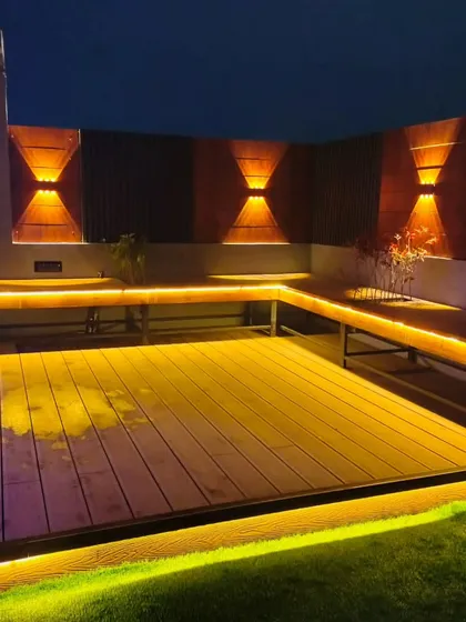 This seating area in Uttam Nagar features a raised wooden deck with built-in L-shaped benches, surrounded by warm, low-level LED strip lighting.