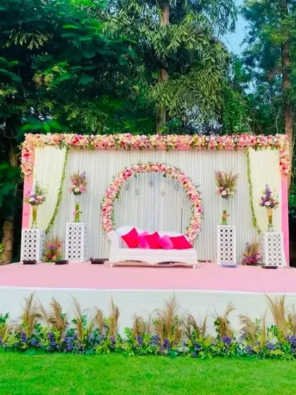 A beautiful pastel pink outdoor stage for a day wedding. The circular floral arch behind the sofa creates a perfect frame for the couple, with pampas grass adding a modern touch.
