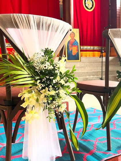 A close-up of the couple's chair decor for a church wedding, showing the detail of the white netting and the fresh floral arrangement.
