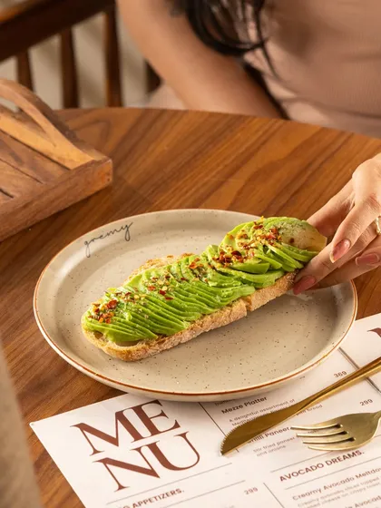 Sliced avocado toast, showing the vibrant green of the avocado. The hand reaching for a slice makes it feel interactive.