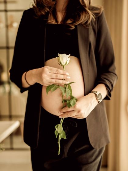 A beautiful and symbolic indoor portrait. The mom-to-be holds a single white rose against her bare bump, a simple and elegant celebration of new life.