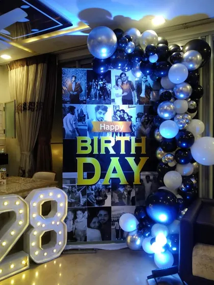 A surprise birthday party at home, made extra special with a personalized photo collage backdrop, a balloon garland, and light-up marquee numbers for the age.