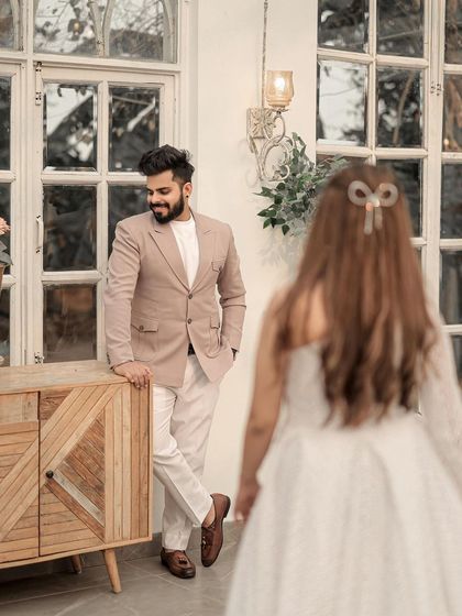 A candid, story-driven shot. The groom waits with a smile as his bride approaches, creating a sense of anticipation and romance in this beautifully lit indoor setting.