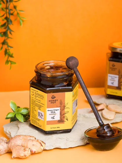 A jar of honey ginger tea concentrate styled with fresh ginger against a vibrant orange background. The bold color choice makes the product stand out.