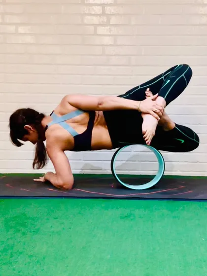 A yoga wheel can be used to add a challenge or provide support in complex poses. Here it assists in a deep, bound leg stretch, showing that props are for holding power, not just for beginners.