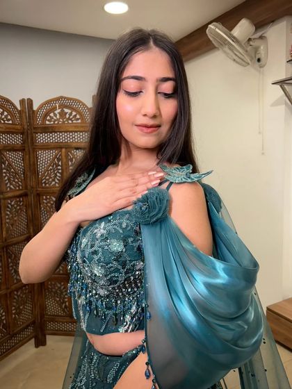 A detailed shot of the unique shoulder embellishment and the flowing cape fabric of the teal gown.