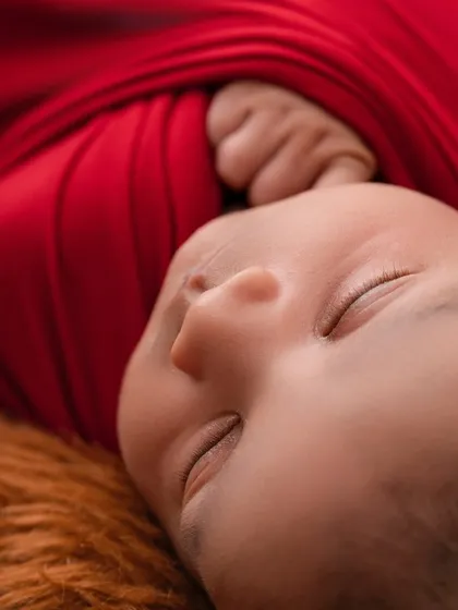 A detailed shot focusing on the tiny hand and peaceful profile of a newborn during the Harry Potter session. I ensure every part of the theme, like the texture of the red wrap, adds to the story while keeping your baby safe and comfortable.