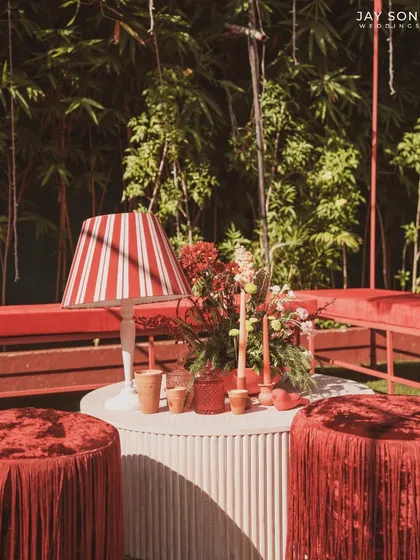 A close-up of a table setting in the "Red Affair" lounge, featuring a striped lampshade and fringed stools that add texture and pattern to the monochromatic space.