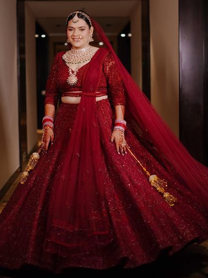 A full-length portrait of the bride, Muskan, in her stunning red wedding lehenga. Her happy smile and the flowing fabric create a joyful and radiant image.