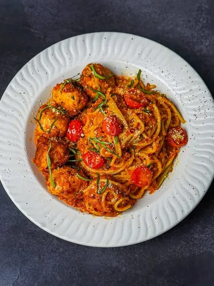 A top-down shot of the spaghetti and meatballs, styled simply on a white plate against a dark surface. This contrast makes the dish the center of attention.