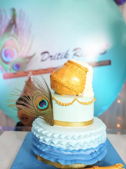 A detailed look at the custom cake for the peacock-themed party. The design includes a golden pot, delicate ruffles, and a real peacock feather, tying it directly into the overall event decoration.