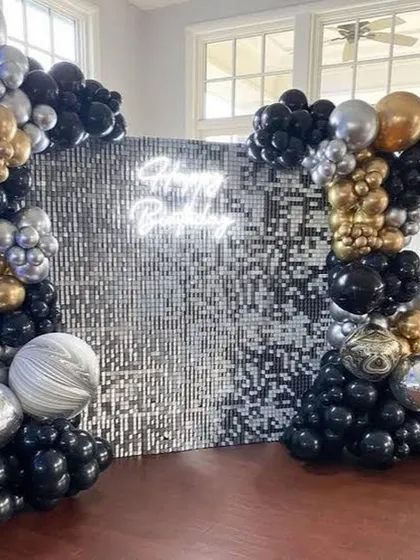 A silver and black sequin wall provides a dazzling photo backdrop. The setup is framed by an organic balloon garland in matching colors, perfect for a stylish birthday party or event.