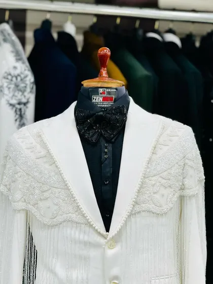 A unique white tuxedo jacket with a heavily beaded and fringed shoulder detail, paired with a black shirt and bow tie. A true showstopper for a fashion-forward client.