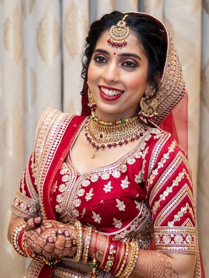 A classic North Indian bridal look in a stunning red lehenga. The makeup is timeless, with a focus on radiant skin, defined eyes, and a bold red lip.