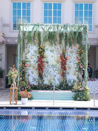 A vertical floral backdrop by the pool, with a botanical print and cascades of real flowers, creating an immersive and vibrant photo spot.