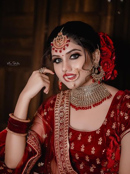 A classic beauty shot of the bride in her red velvet lehenga. Her pose is elegant, and she looks directly at the camera with a confident and alluring expression.