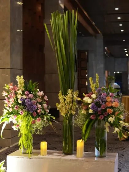 Elegant floral arrangements with tall greenery in glass vases, placed on white pedestals to greet guests.